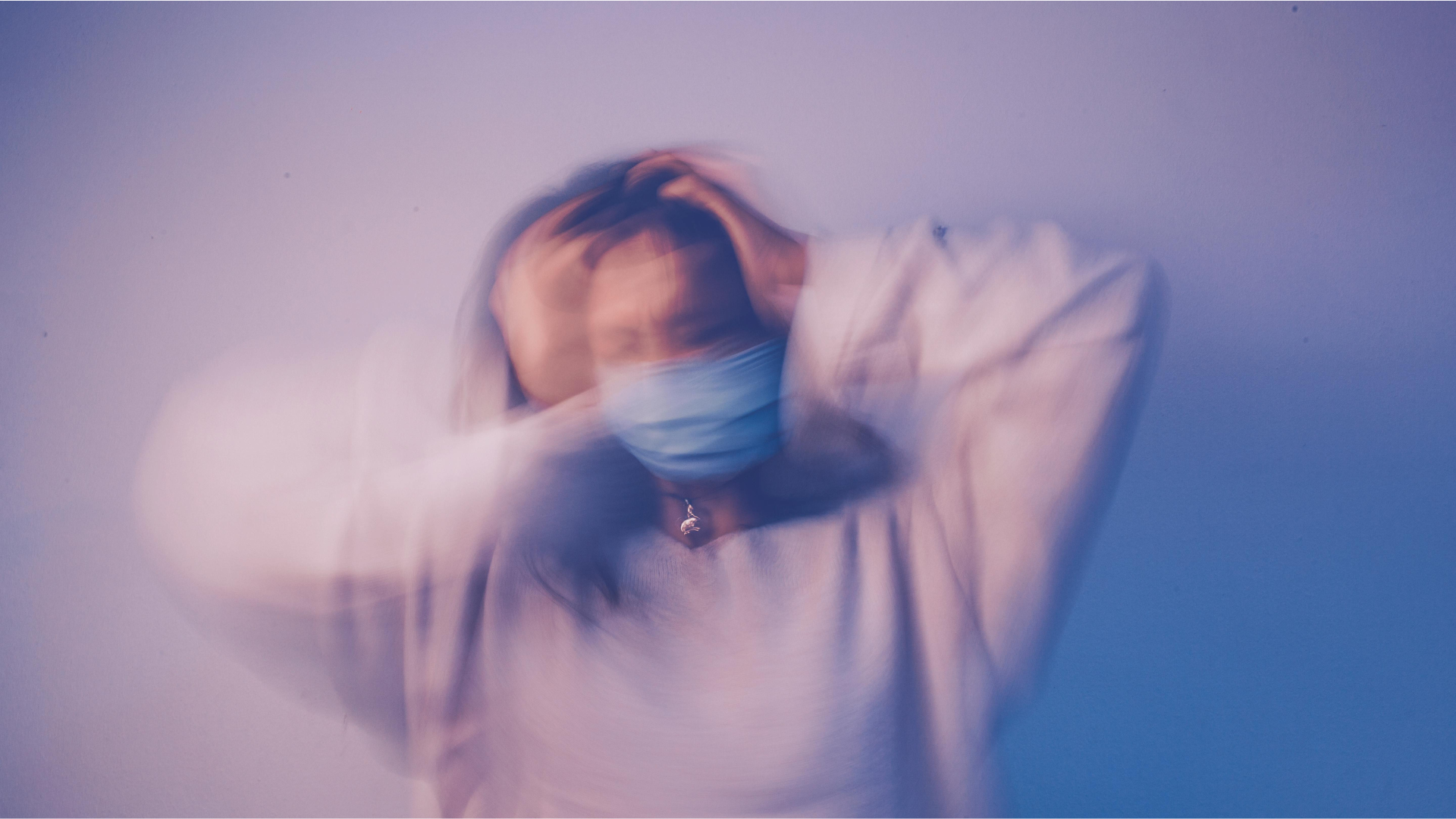 Motion-blurred person in mask clutching head, visualizing the disorientation of severe anxiety.