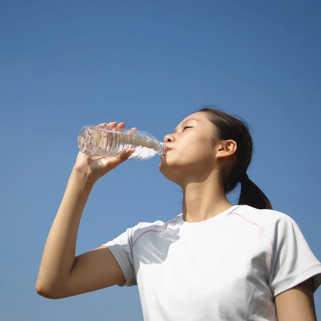 Adequate hydration: woman drinking filtered water outdoors under a clear sky to support healthy hormone balance.